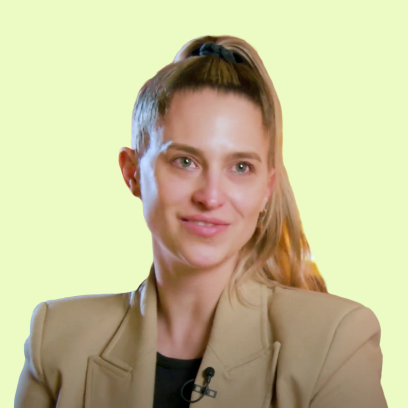 Eine Person mit Pferdeschwanz lächelt vor grünem Hintergrund