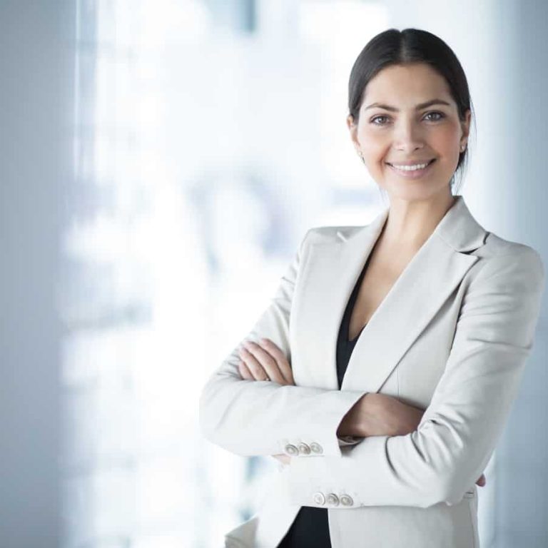 Selbstbewusste Frau in Businesskleidung mit verschränkten Armen vor hellem Hintergrund