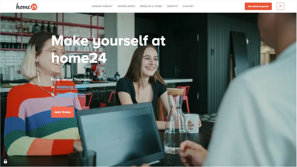 Drei Menschen im Gespräch in einem modernen Café, lachend und mit Laptops.