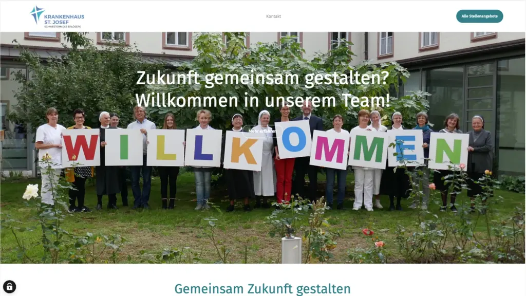 Gruppenfoto von Mitarbeitern hält bunte "WILLKOMMEN" Schilder vor einem Krankenhausgebäude