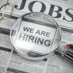 Das Bild zeigt eine Zeitung mit Stellenanzeigen und einer Lupe darüber.