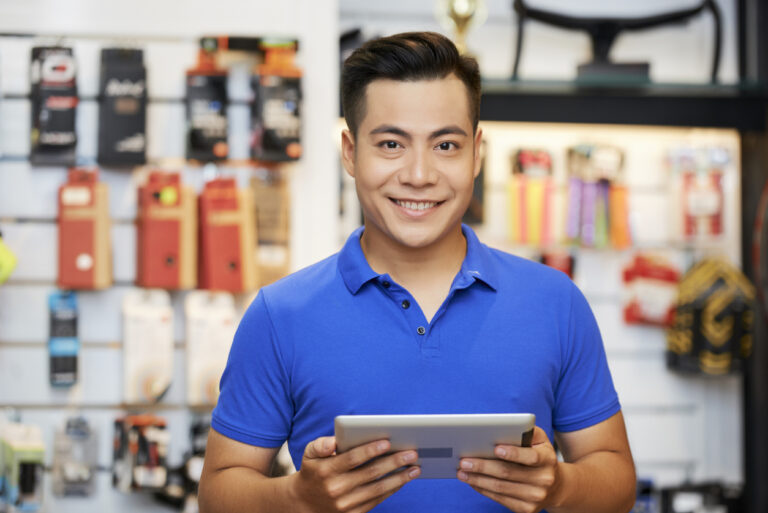 Porträt eines Verkäufers, der in einer Werkstatt mit einem digitalen Tablet steht und in die Kamera lächelt