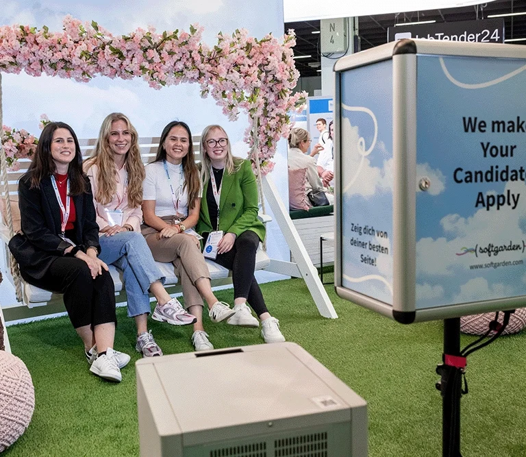 Vier Besucher*innen des softgarden Stand sitzen auf der Hollywoodschaukel und lächeln in die Kamera der Fotobox