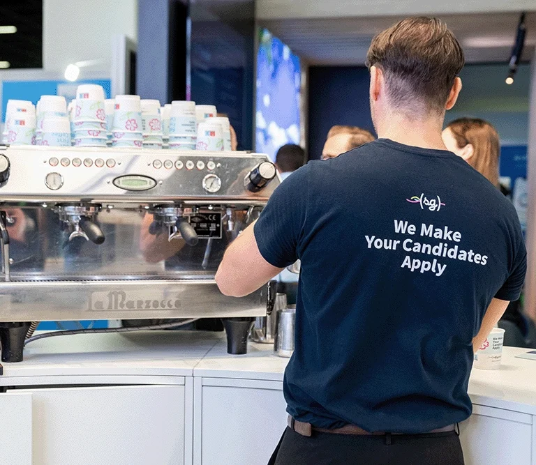 Ein*e Mitarbeiter*in der Cafébar steht vor einer großen Siebträger-Kaffeemaschine und bereitet einen Kaffee zu